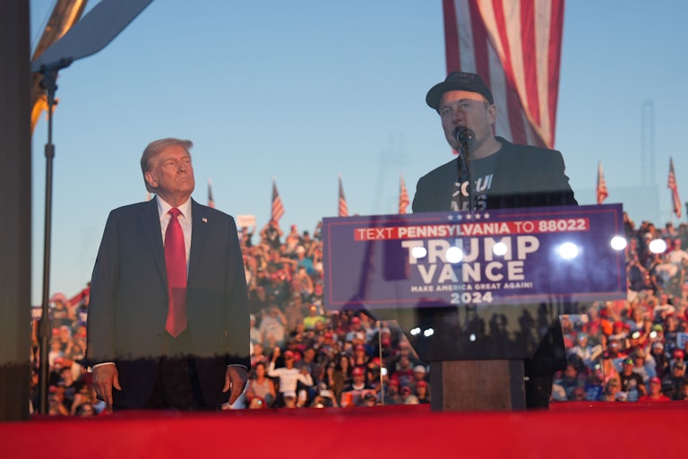 Donald Trump looks on while Elon Musk speaks at a podium