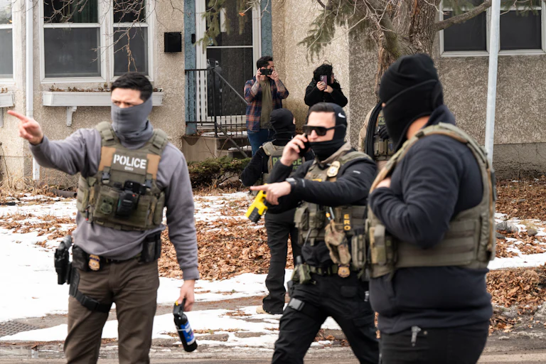 Federal immigration agents stand in a residential street. One of them points to the side.