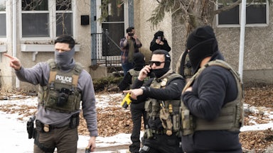 Federal immigration agents stand in a residential street. One of them points to the side.