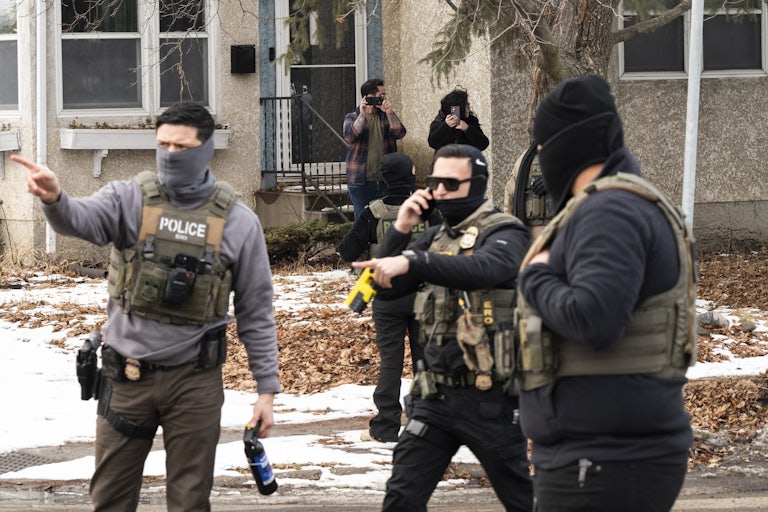 Federal immigration agents stand in a residential street. One of them points to the side.