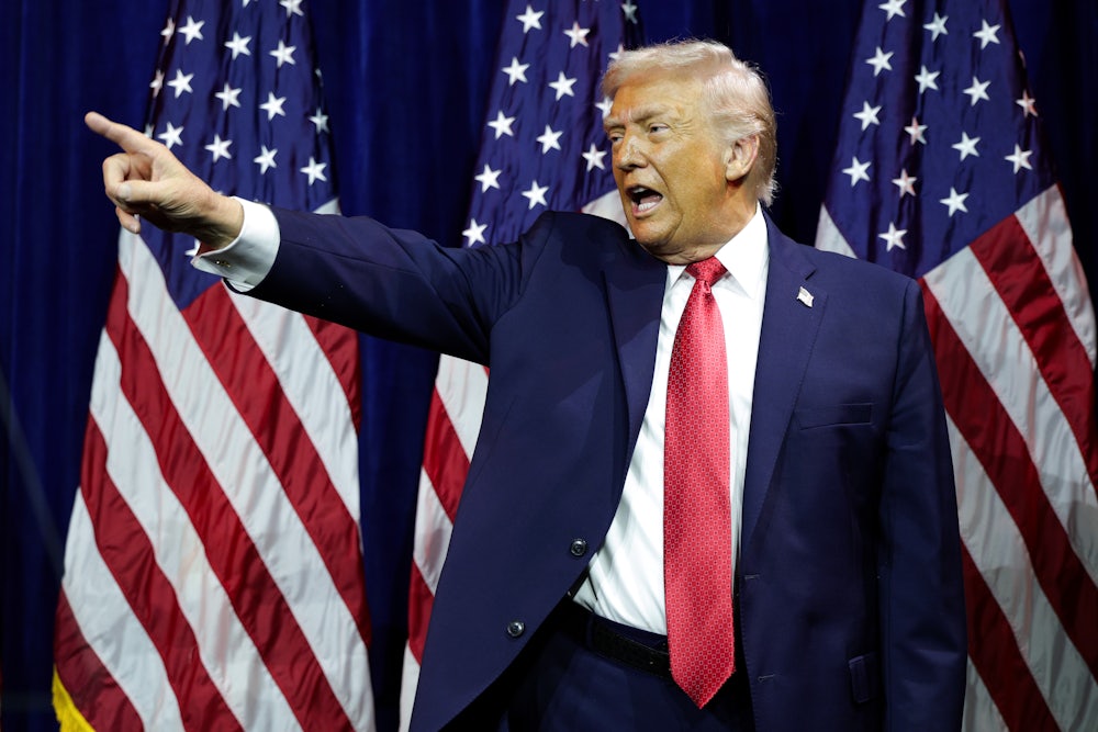 Donald Trump points and yells in front of several American flags