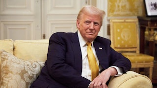 Trump sits, leaning on the arm of an upholstered sofa.