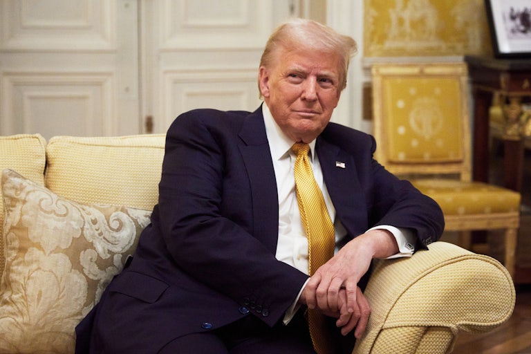 Trump sits, leaning on the arm of an upholstered sofa.