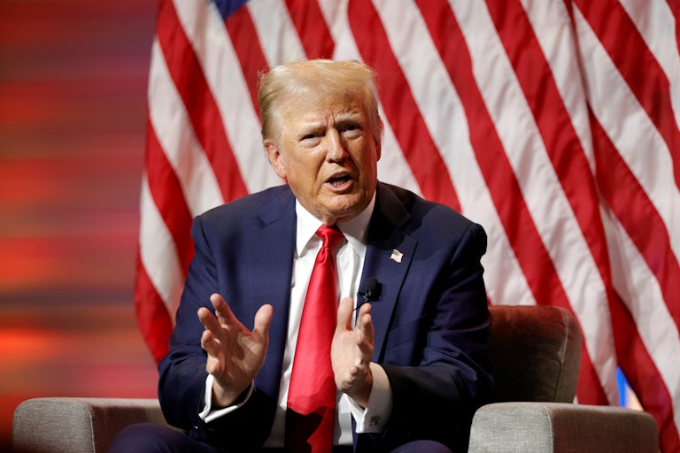 Donald Trump sits on an armchair and speaks, hands splayed outward