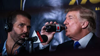 Donald Trump drinks a bottle of Diet Coke while sitting next to his son Donald Trump Jr.