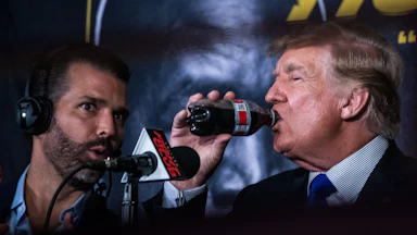 Donald Trump drinks a bottle of Diet Coke while sitting next to his son Donald Trump Jr.