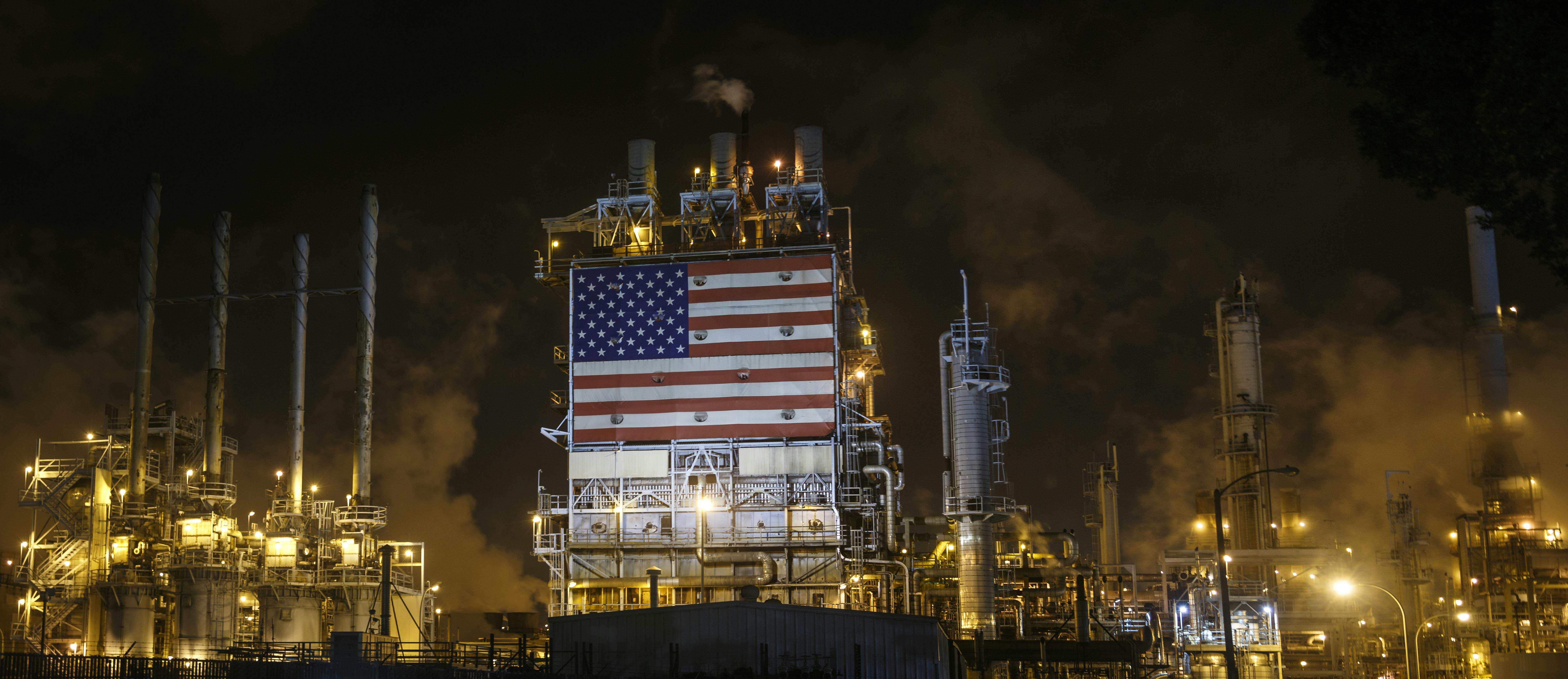 An American flag is displayed among smokestacks and lights.