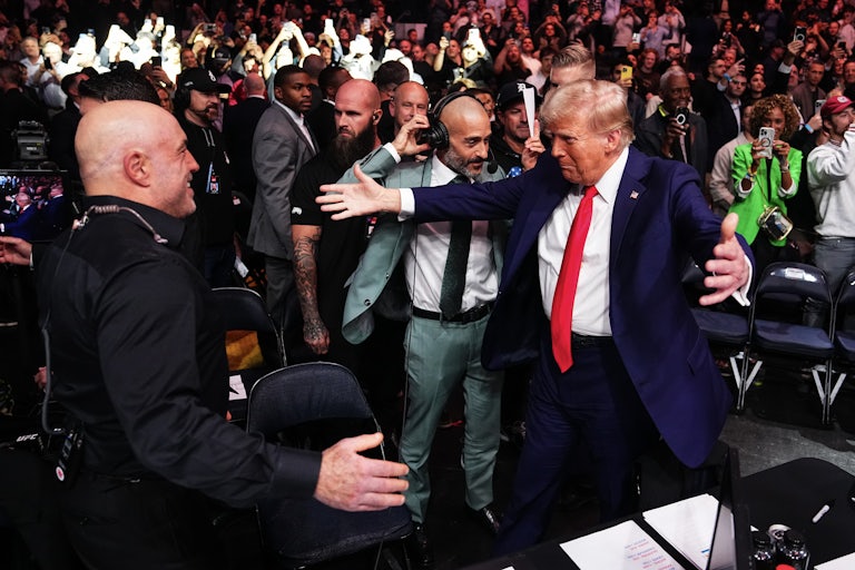 Joe Rogan greets Donald Trump during the UFC 309 event at Madison Square Garden on November 16, 2024. Trump spreads his arms outward for a big hug, while Rogan smiles.
