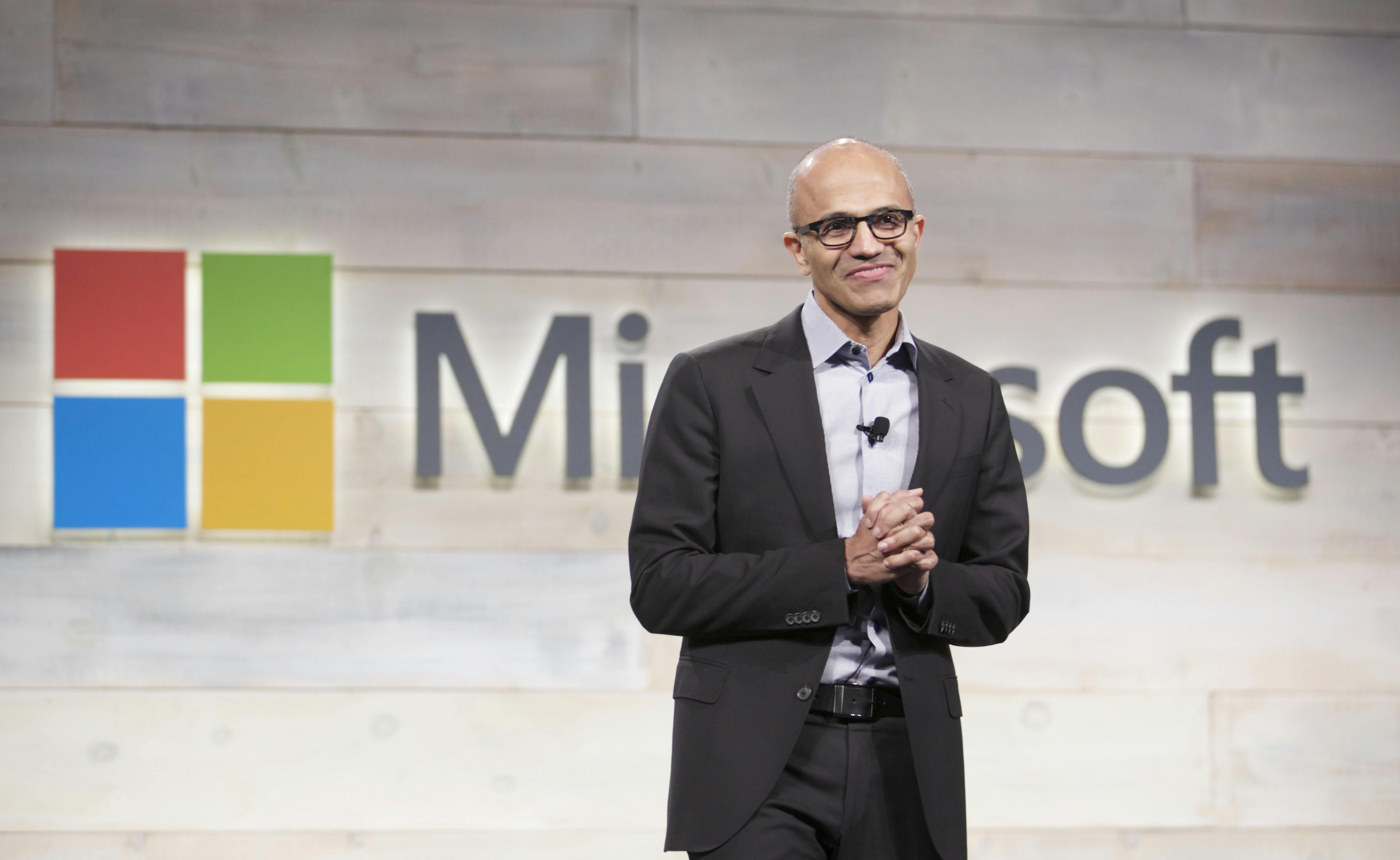Microsoft CEO Satya Nadella speaks in front of a Microsoft logo.