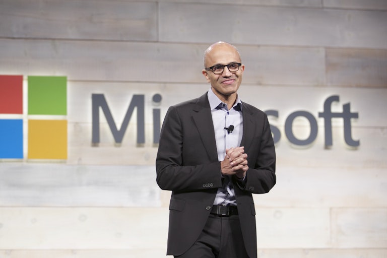 Microsoft CEO Satya Nadella speaks in front of a Microsoft logo.