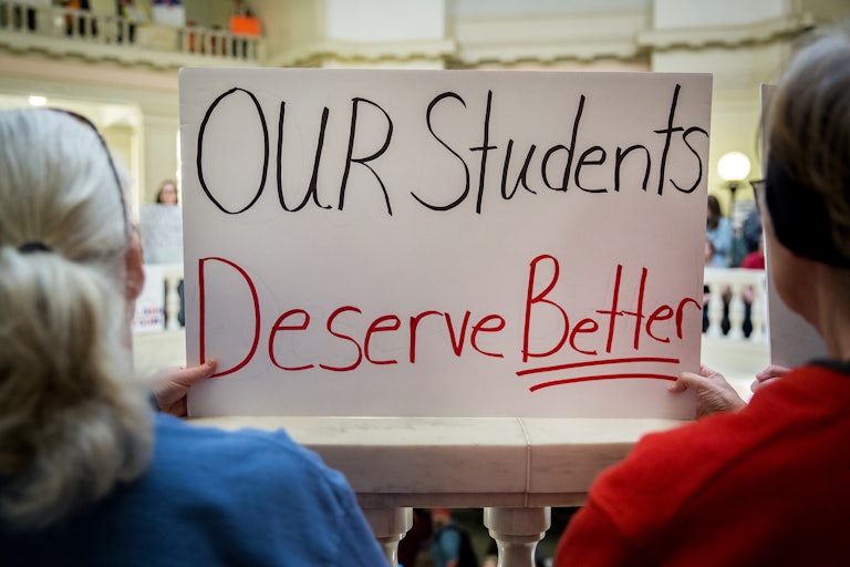 Two people hold up a sign that says, "Our students deserve better"