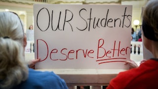 Two people hold up a sign that says, "Our students deserve better"