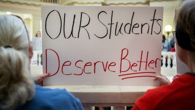 Two people hold up a sign that says, "Our students deserve better"