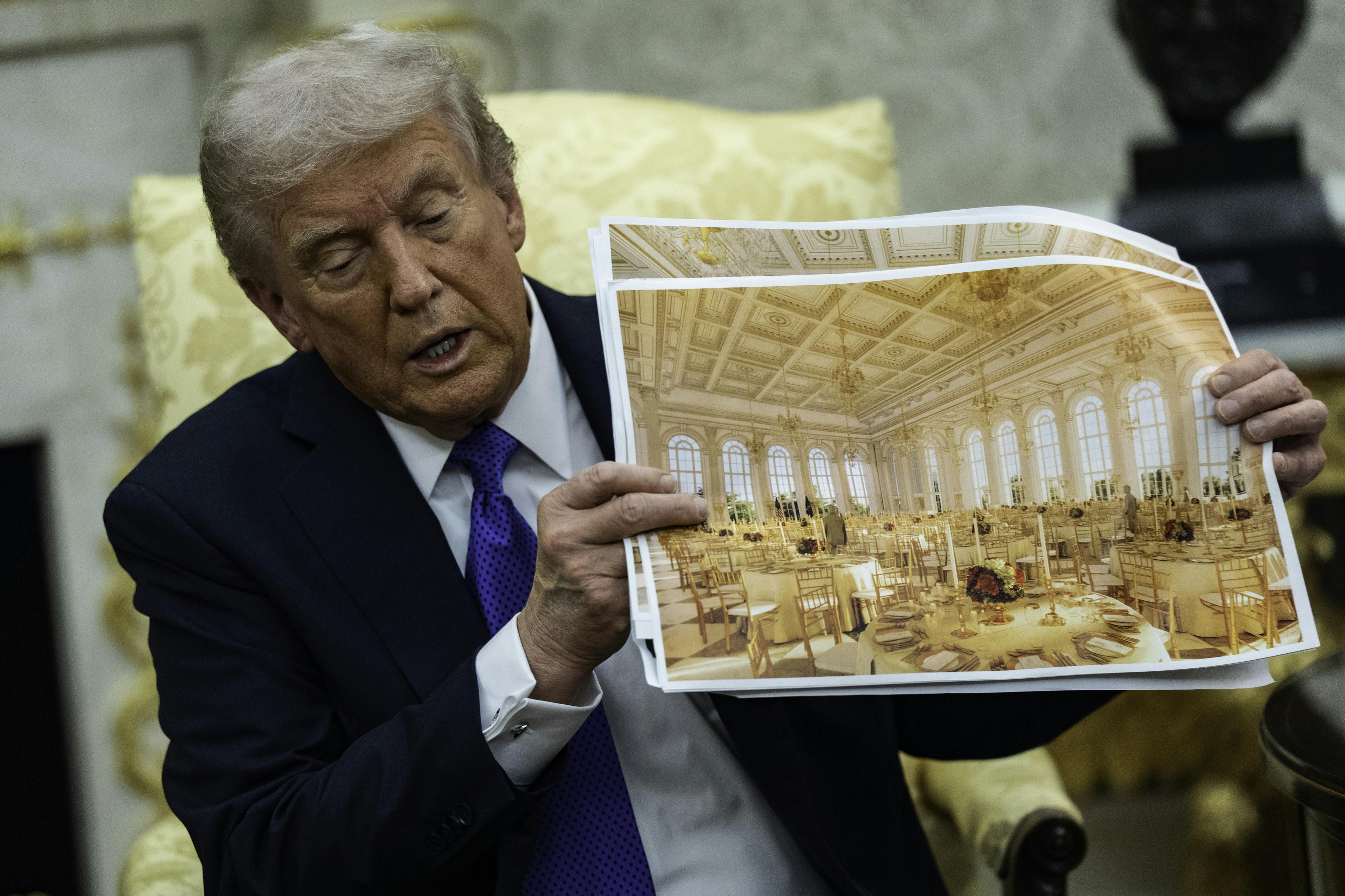 Donald Trump speaks and holds up renderings of his ballroom while sitting in the Oval Office