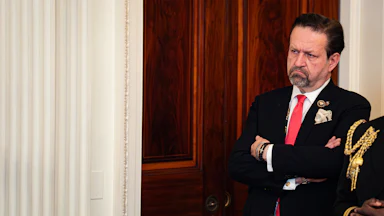 Sebastian Gorka frowns and stands with his arms crossed during an event at the White House