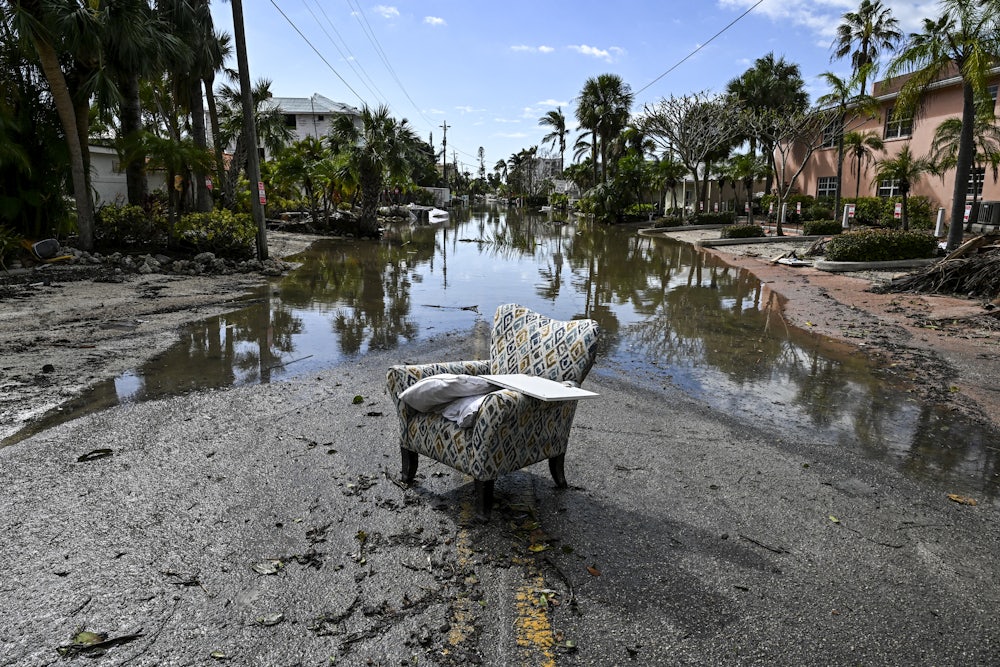 This image shows a street with standing water and mood, with an arm chair in the middle of it.