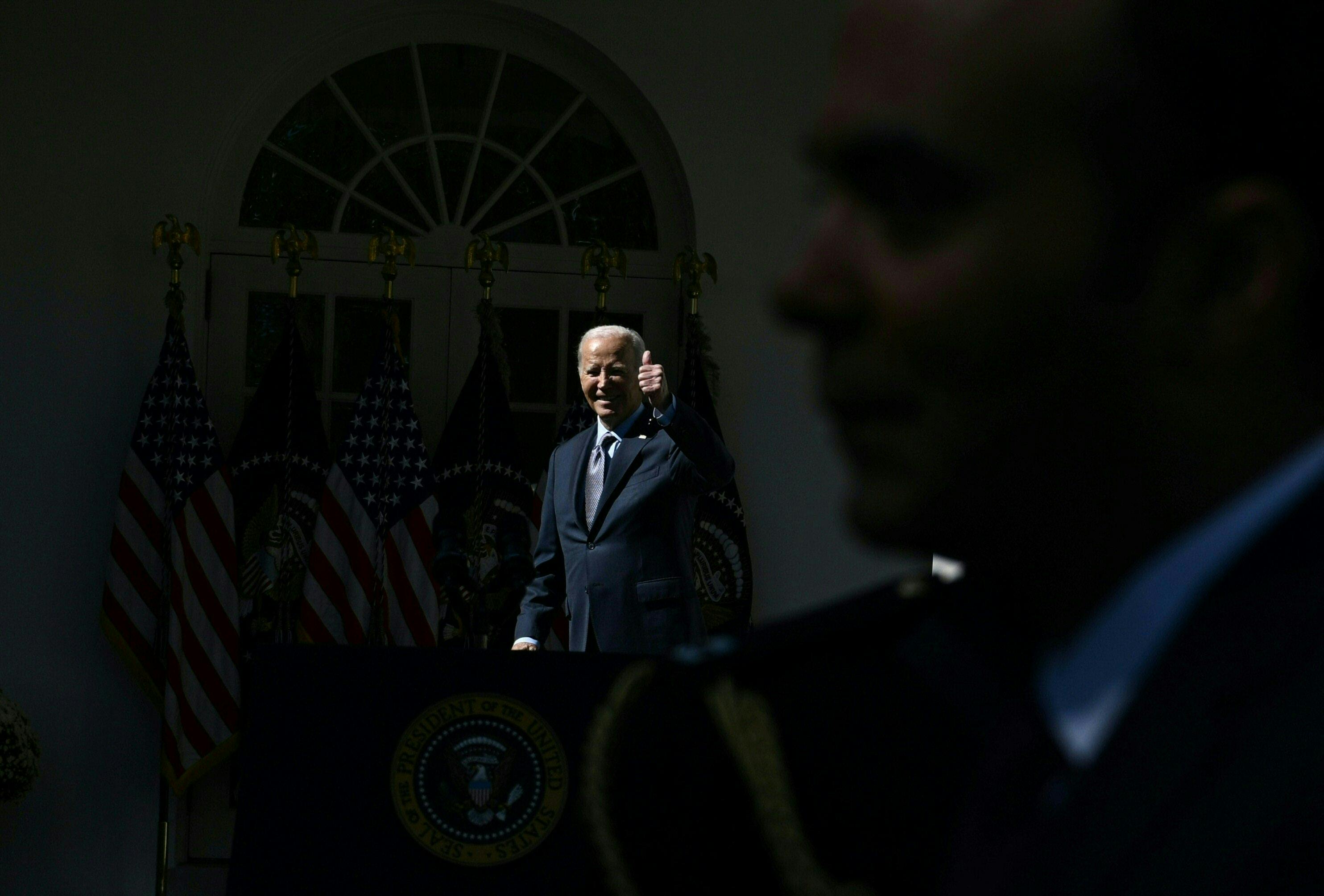 Joseph Biden gives a thumbs up in the darkness as a man blocks a camera. 