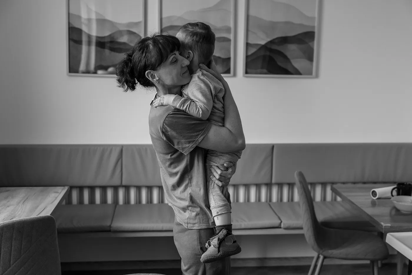 A black and whtte photo of Liudmyla Popravka, a Ukrainian woman from Sumy, hugged her two-year-old son, Eldar, in the kitchen of the Jesuit refugee housing center.