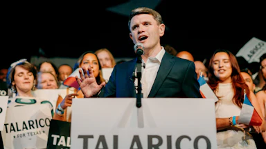 Talarico stands at a podium reading "TALARICO FOR TEXAS," speaking into a microphone as supporters stand behind him.