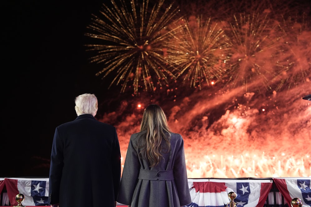 The Trumps hold hands before American flag decorations and a fireworks display that leaves most of the sky awash in flame and smoke.