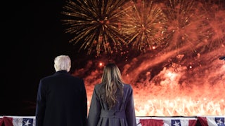 The Trumps hold hands before American flag decorations and a fireworks display that leaves most of the sky awash in flame and smoke.