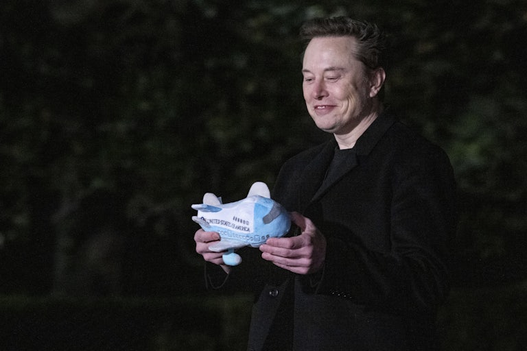 Elon Musk looks down at a stuffed airplane that he is holding