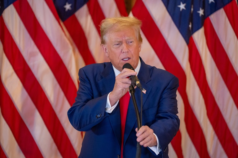 Donald Trump speaks before a mic. U.S. flags are behind him.