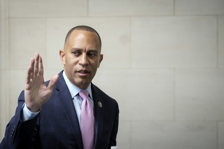 Hakeem Jeffries, wearing a dark suit and a light purple tie, raises his hand as he walks in the Capitol.
